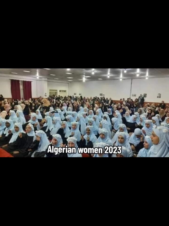 A large gathering of Algerian women and girls in 2023, the majority in matching light blue hijabs, in what appears to be a school auditorium.