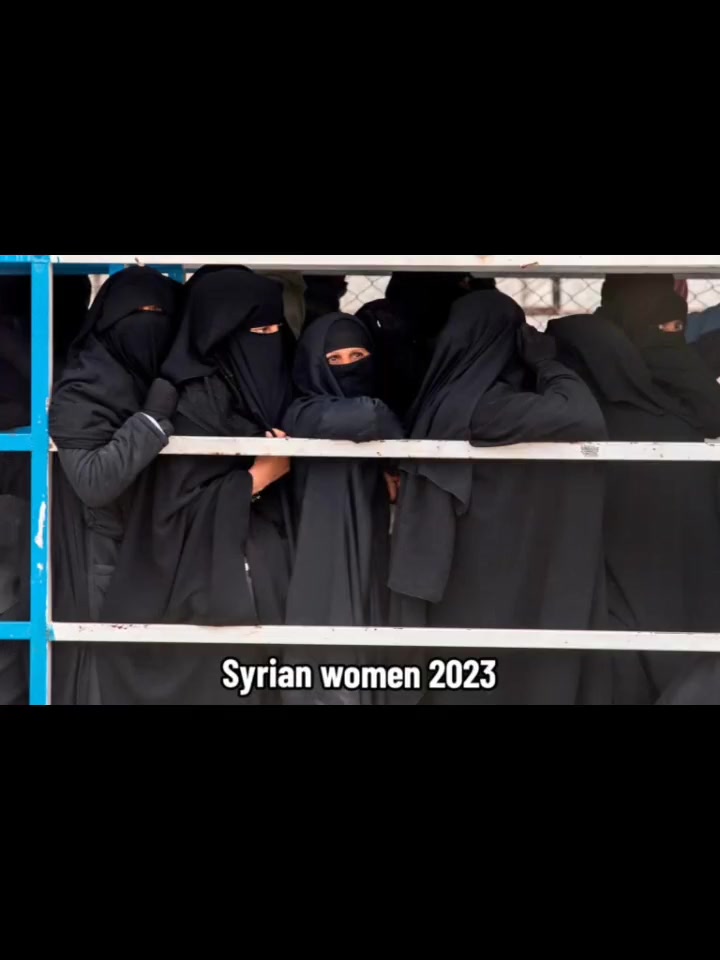 Syrian women in 2023 in full black niqab, crowded together against a fence.